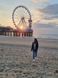 Woman with ferris wheel at beach against sky during sunset