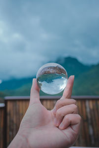 Cropped hand holding crystal ball against sky