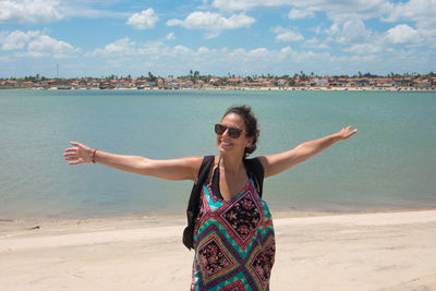 Smiling woman with arms outstretched standing at beach