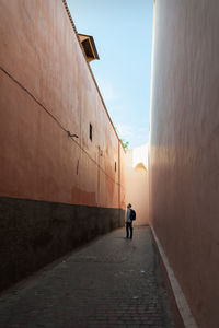 Rear view of man walking on footpath amidst buildings
