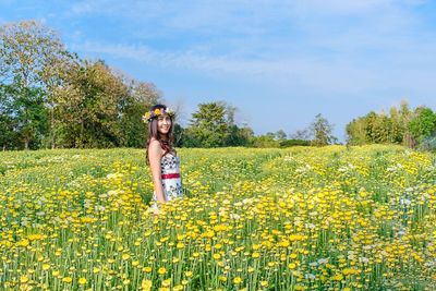 Full length of woman standing by yellow flowers on field