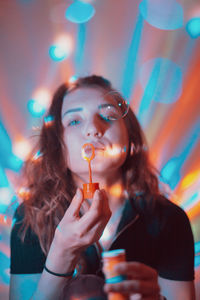 Portrait of woman blowing bubbles against illuminated lights