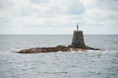 Lighthouse on rock by sea against sky