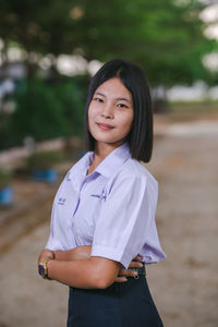 Confident school girl with arms crossed standing outdoors