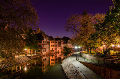 Illuminated buildings by canal against sky at night