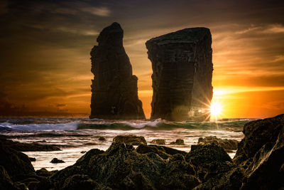 Rock formation on beach against sky during sunset