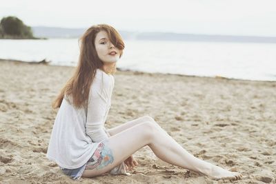 Young woman sitting on beach against sky