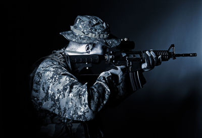 Side view of man holding gun in dark at night