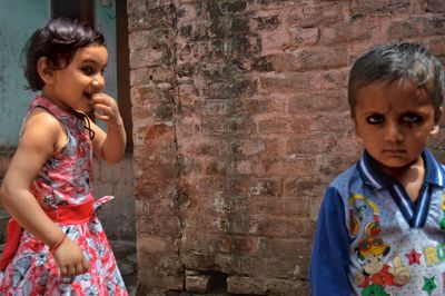 Portrait of boy with sister standing against brick wall