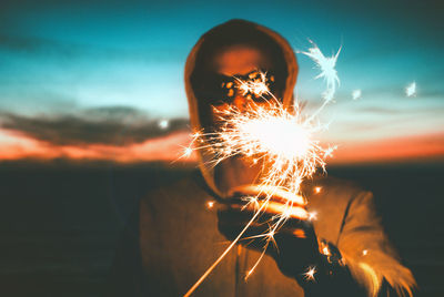 Close-up of hand holding sparkler at sunset