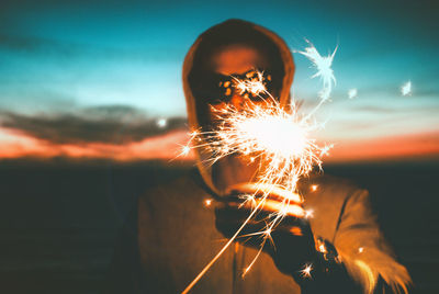 Close-up of man with lit sparkler during sunset