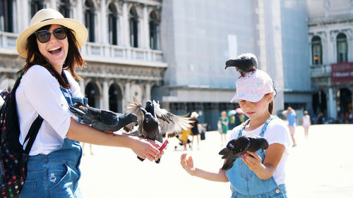 View of happy woman and kid girl, tourists, holding pigeons, feeding, play with them