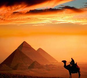 Man riding camel by pyramids against orange sky