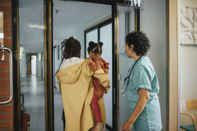 Female doctor walking behind woman carrying daughter while walking in corridor of hospital