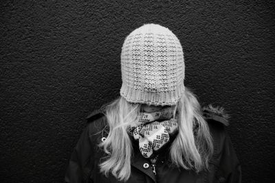 Woman face covered with knit hat while standing against wall