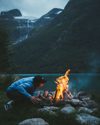 Person with fire on rock by lake