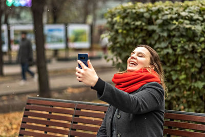 Smiling woman videochat by smartphone sitting on a bench.video call to a mobile phone.