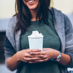 Midsection of smiling woman holding coffee cup with whipped cream in city