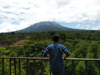 Rear view of man looking at mountains against sky