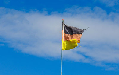 Low angle view of torn german flag against blue sky