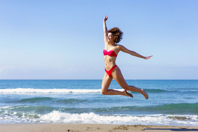 Full length of woman jumping at beach against sky