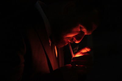 Close-up of man holding lit candle in dark
