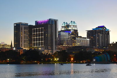 Illuminated buildings by river against sky in city