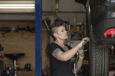 Hipster female mechanic repairing car's wheel in auto repair shop