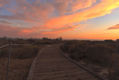 Scenic view of boardwalk on beach against sky during sunset