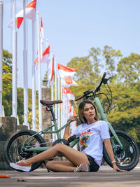 A woman is sitting on the floor with her bicycle.