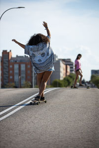 Young and afro woman skating long board by an empty bridge at sunset, back view