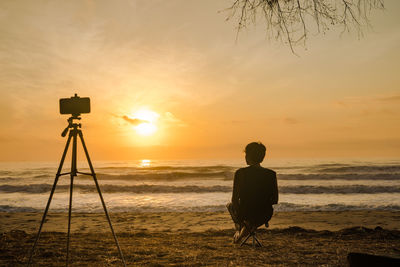Silhouette phone on tripod and man sit on beachchair take photo beach with sunrise and sea 