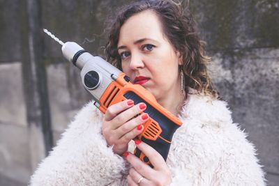 Portrait of confident young woman holding drill machinery