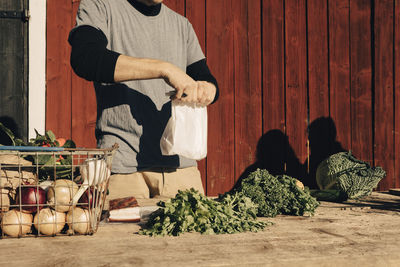 Midsection of mid adult male farmer holding paper bag with vegetables on table