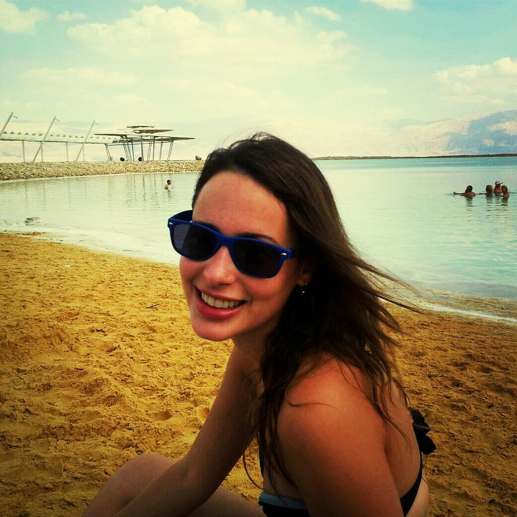 beach, young adult, sunglasses, portrait, person, looking at camera, young women, sea, lifestyles, leisure activity, water, sky, smiling, shore, sand, front view, vacations