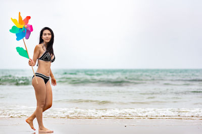 Full length of woman holding pinwheel toy while walking at beach