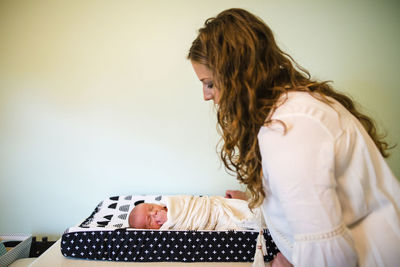 Side view of mother looking at newborn son against wall at home