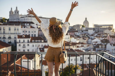 Rear view of woman standing with arms outstretched against cityscape