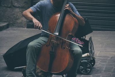 Midsection of street musician playing cello on footpath
