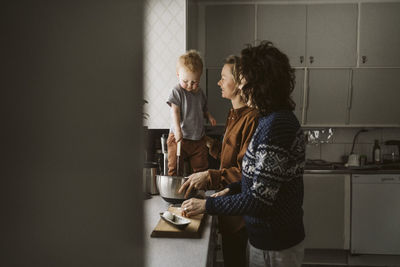 Gay couple preparing food with daughter standing on kitchen counter at home