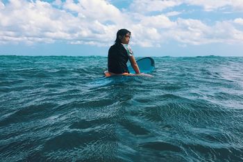 Girl with surfboard in sea against sky