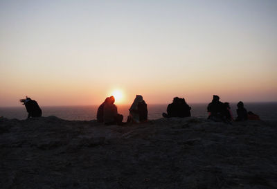 People sitting on rocks against sea during sunset