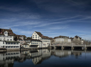 Bridge over river by buildings against sky in city