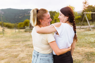 Side view of cheerful friends embracing while standing on land