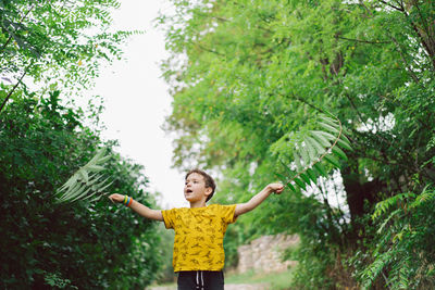 A six-year-old boy runs with green leaves in his hands in the countryside.