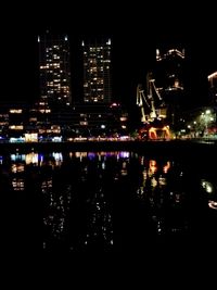 Illuminated buildings by river against sky at night