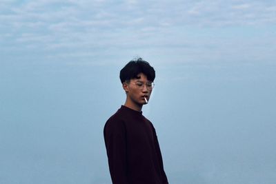 Young man smoking cigarette against sky