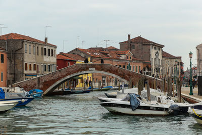 Sailboats moored on sea by buildings in city against sky