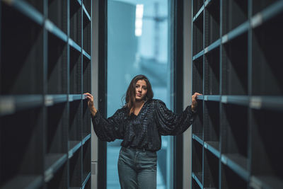 Portrait of young woman standing amidst shelves