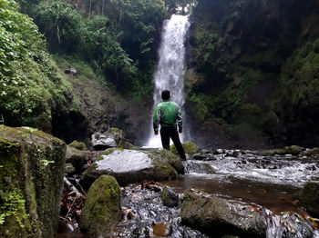 Rear view of man standing against waterfall in forest